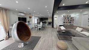 Un salon moderne avec une table à manger en verre, un canapé, une table basse et un grand fauteuil rond en métal.