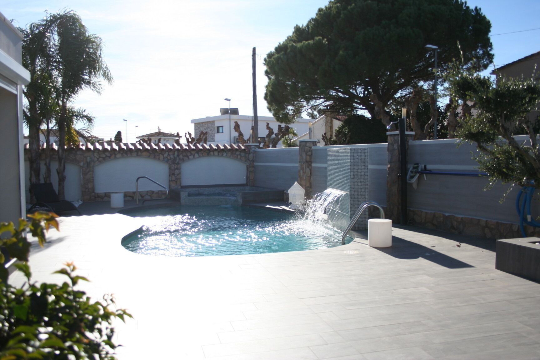 Une piscine agrémentée d’une cascade, entourée de murs de pierre et d’arbres.