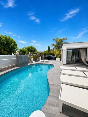 A swimming pool with a curved edge, lounge chairs, and a covered seating area.