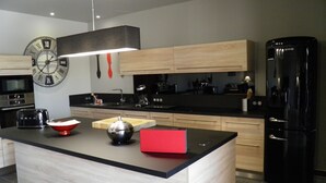Eine moderne Küche mit einer zentralen Kochinsel, Holzschränken, einem schwarzen Kühlschrank, einer Uhr und einer Kaffeemaschine.