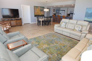 A living room with a sofa, chairs, a coffee table, a TV, and a dining area with chairs and a table. - Experience the amazing views at Condo 601 - a spacious 3BR ocean view retreat in South Padre Island. (South Padre Island)