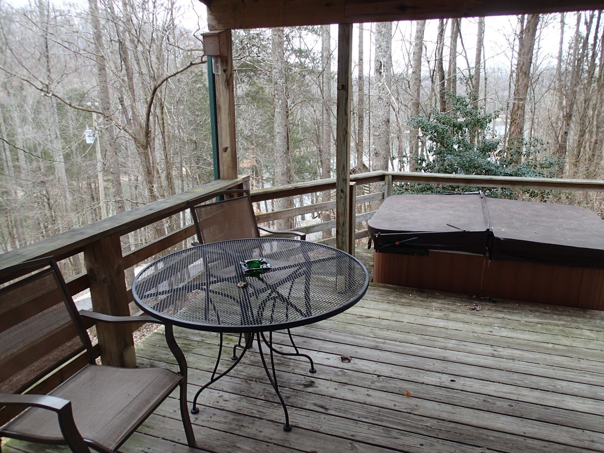 A wooden deck with a metal table and chairs, a hot tub, and a view of a forest.