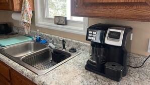 Een keuken met een roestvrijstalen spoelbak, een koffiezetapparaat en houten keukenkastjes.