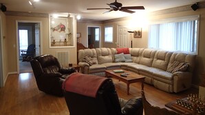 Een woonkamer met een modulaire bank, een leren fauteuil, een houten salontafel en een plafondventilator.