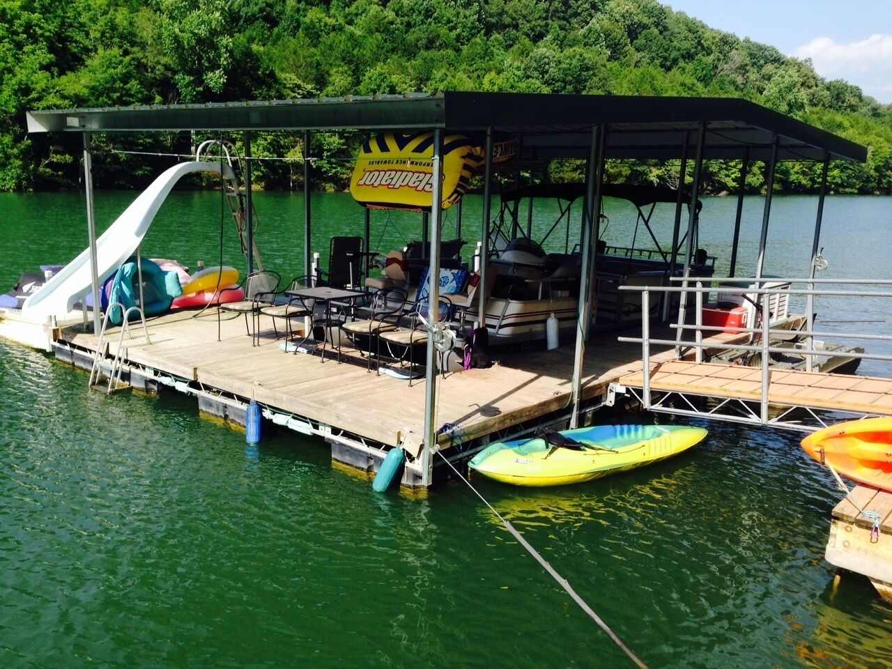 A dock with a covered seating area, a boat ramp, and several kayaks and a canoe.