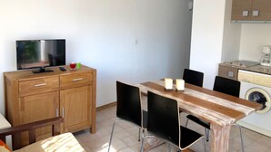 Ett kompakt bostadsutrymme med ett träskåp, en TV, ett matbord med stolar och en tvättmaskin.