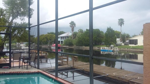 A pool area with a view of a calm lake, a dock, and surrounding greenery. - Waterfront home on deep water canal (Hernando Beach)