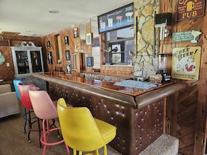 Un espace bar avec un comptoir en bois, des tabourets et divers panneaux, dont un qui indique les « offres spéciales du Flamingo Lounge ».