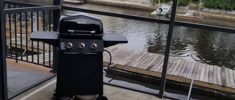 A poolside area with a grill, a dock, and a view of a house across the water.