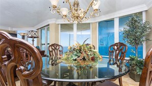 A dining area with a round glass table, ornate chairs, a chandelier, and a view of the sea through large windows. - Corner Penthouse - 1101 - Direct Ocean Front with views of Ocean and Intercostal (Daytona Beach)
