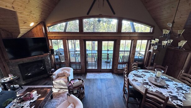 Interior acogedor de una cabaña con chimenea, asientos cómodos, una mesa de comedor y ventanas amplias con vistas al exterior.