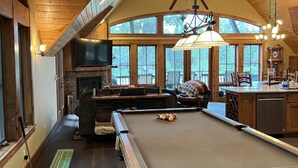 Una habitación acogedora con mesa de billar, techo de madera, ventanas amplias y chimenea.