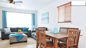 A living room with a sofa, ottoman, and dining table with chairs. - New Carlsbad Beach house - Blocks from beach with rare  cental Air Conditioning (Carlsbad)