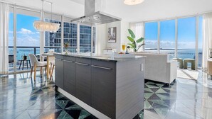 A modern kitchen with a large island, large windows, and a view of the sea.