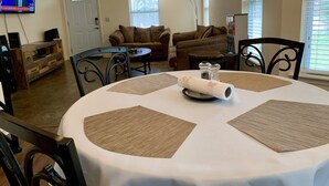 A living room with a round table, brown placemats, a salt and pepper set, and a television displaying a news program. - Discover Oxford Charm, Just A Quick 5-min Drive To University of Mississippi
 (Oxford)