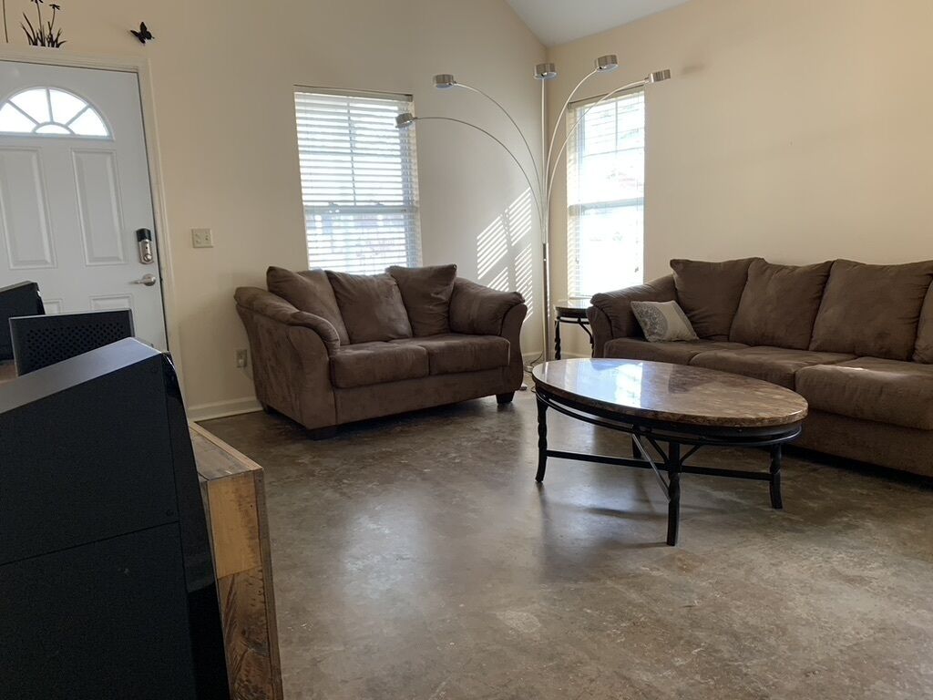 A spacious living room with two brown sofas, a round coffee table, and a TV on a stand.