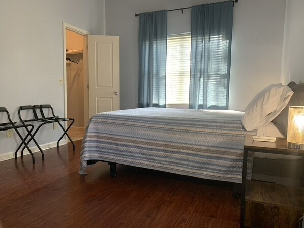 A bedroom with a bed, a chair, a desk with a lamp, and a closet.