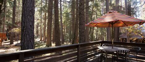 A wooden deck with a table and chairs, surrounded by tall trees.