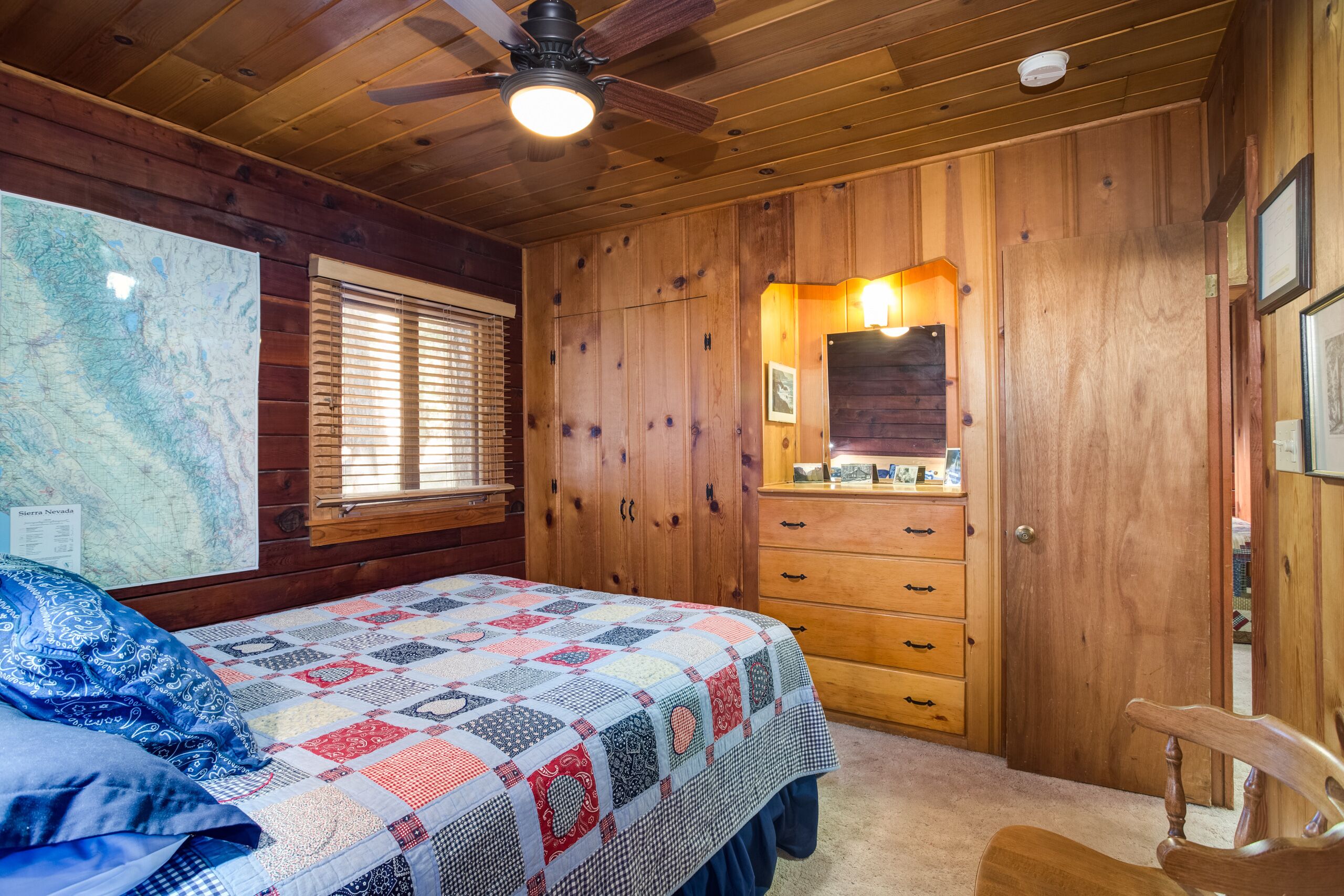 A bedroom with a wooden ceiling, a bed with a quilt, a dresser, and a map on the wall.