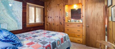 A bedroom with a wooden ceiling, a bed with a quilt, a dresser, and a map on the wall.