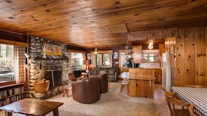 A cozy cabin interior with a stone fireplace, wooden furniture, and a kitchen area. - (53) Creekside Cabin at The Redwoods In Yosemite (Yosemite National Park)