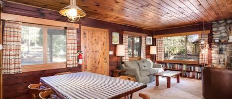 Acogedor interior de cabaña con una mesa de comedor de madera, sillas, un sofá y una chimenea.