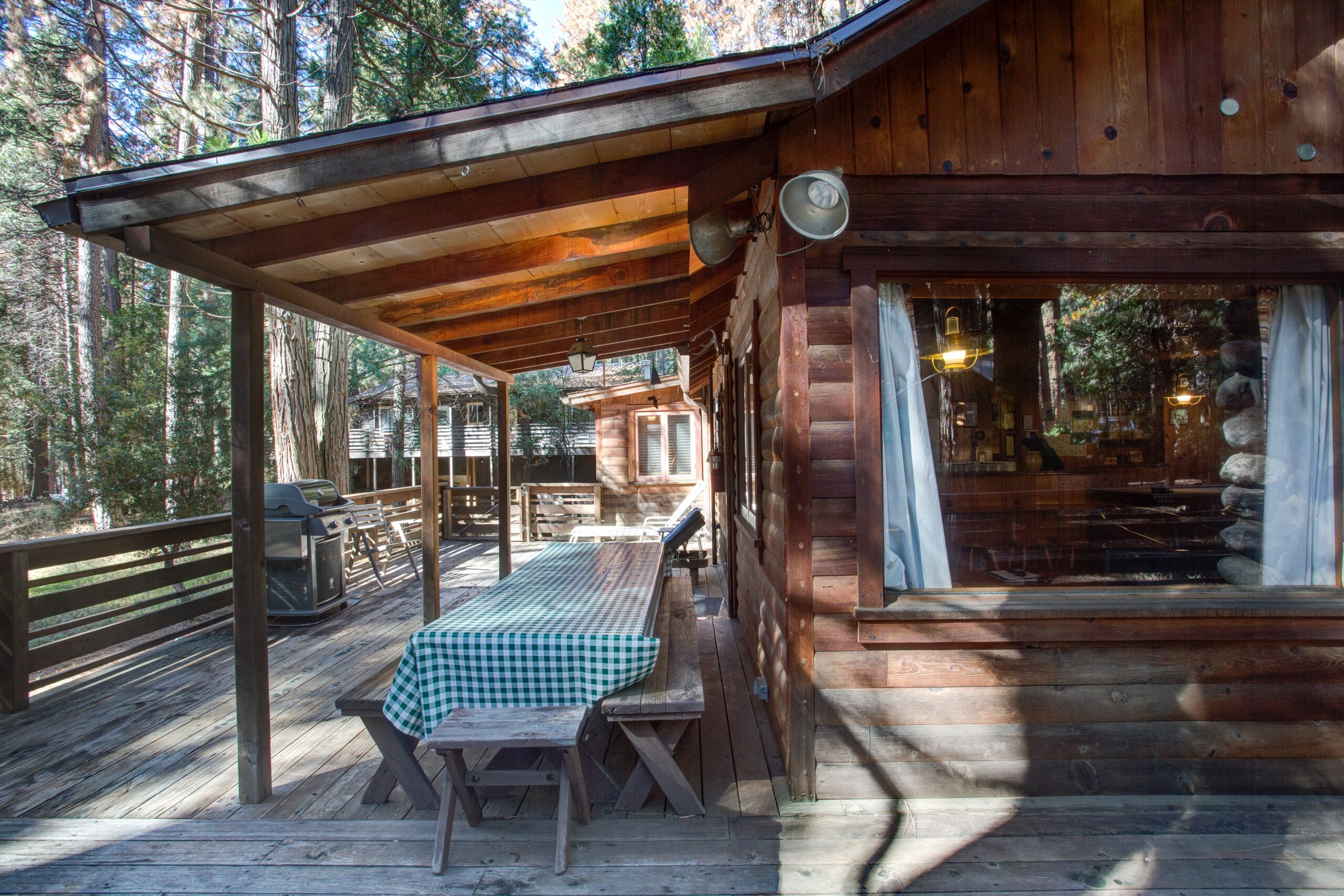 Una cabaña de madera con terraza techada, mesas de picnic y una parrilla.