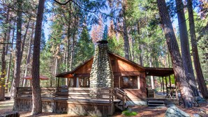 A rustic cabin with a stone chimney, wooden deck, and a covered porch. - (53) Creekside Cabin at The Redwoods In Yosemite (Yosemite National Park)