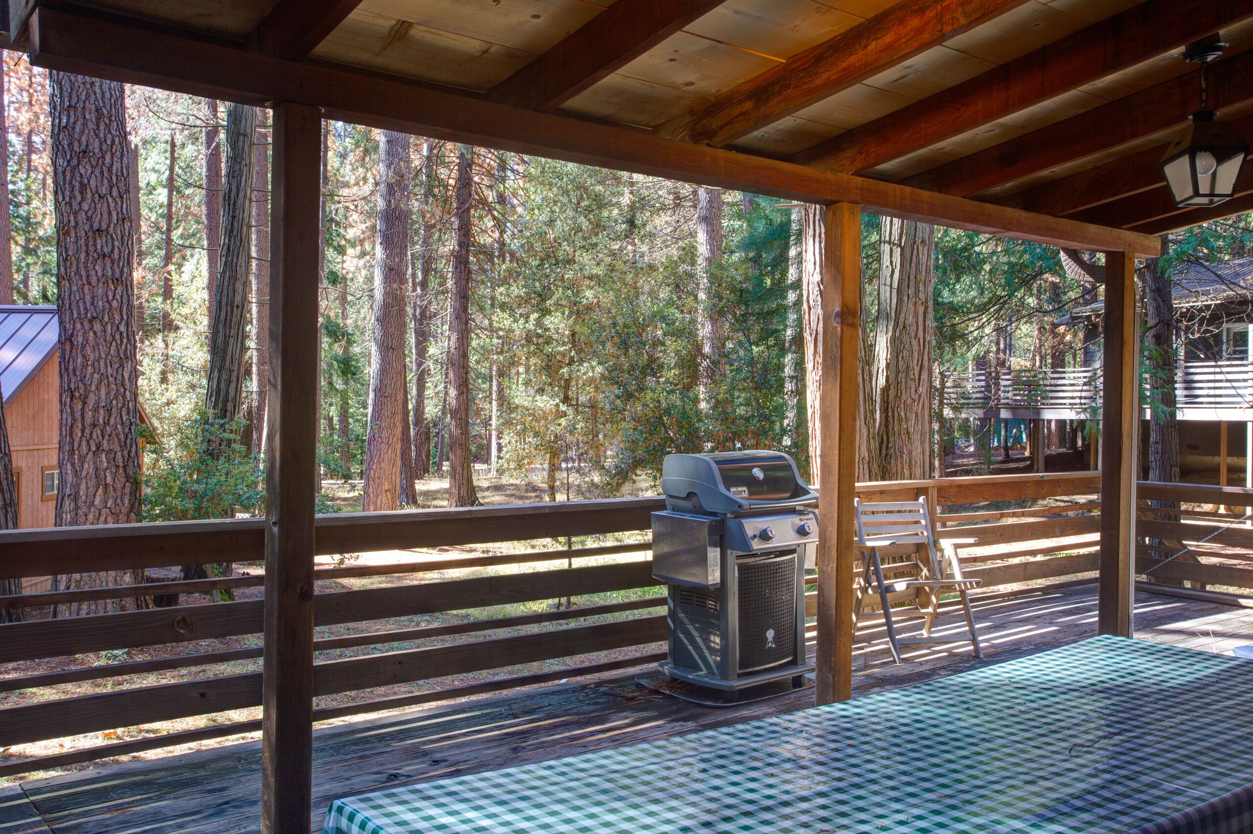A covered outdoor area with a grill, a checkered table, and a wooden bench.