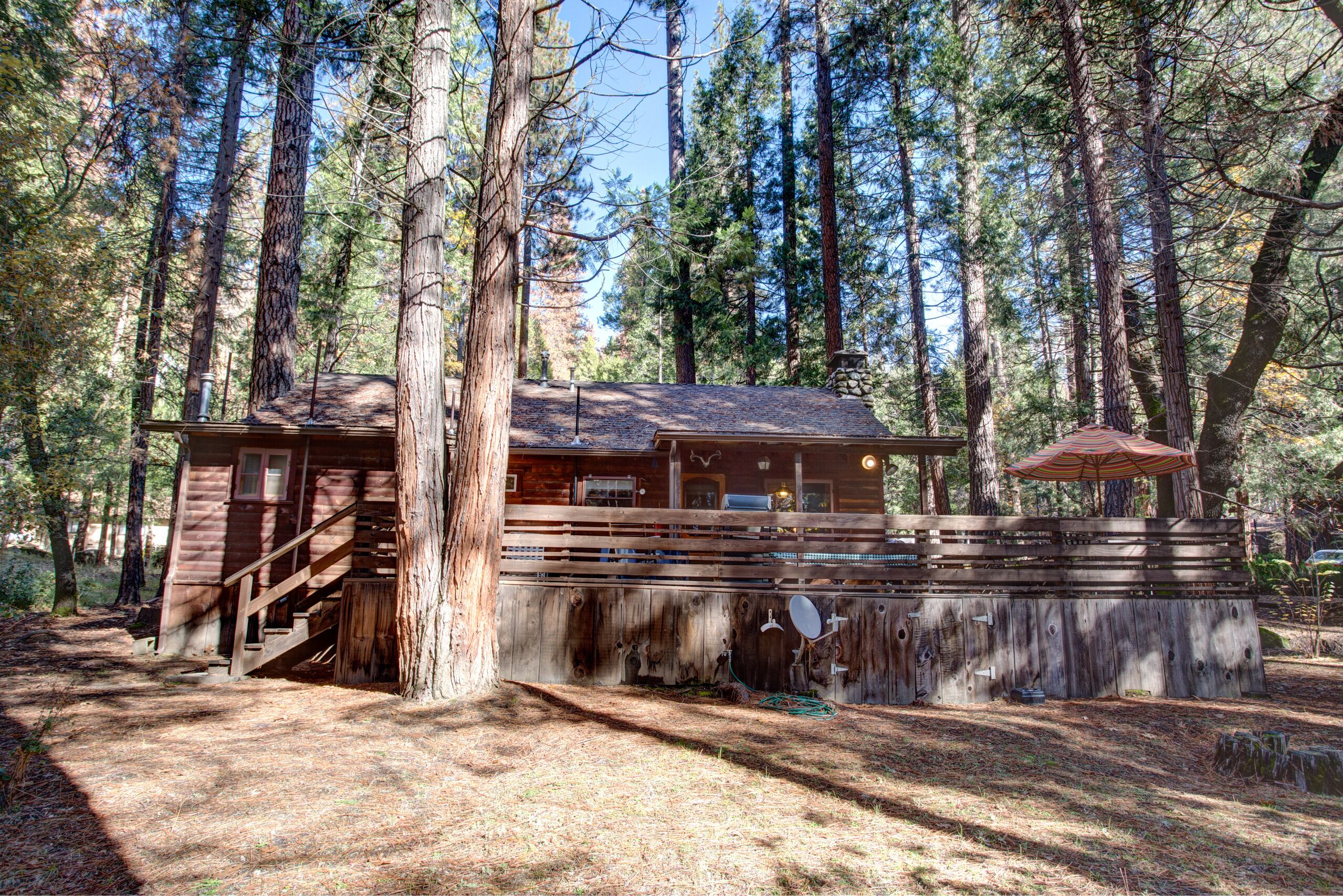 A rustic cabin with a wooden exterior, a staircase leading to the entrance, and a covered area with a red umbrella.