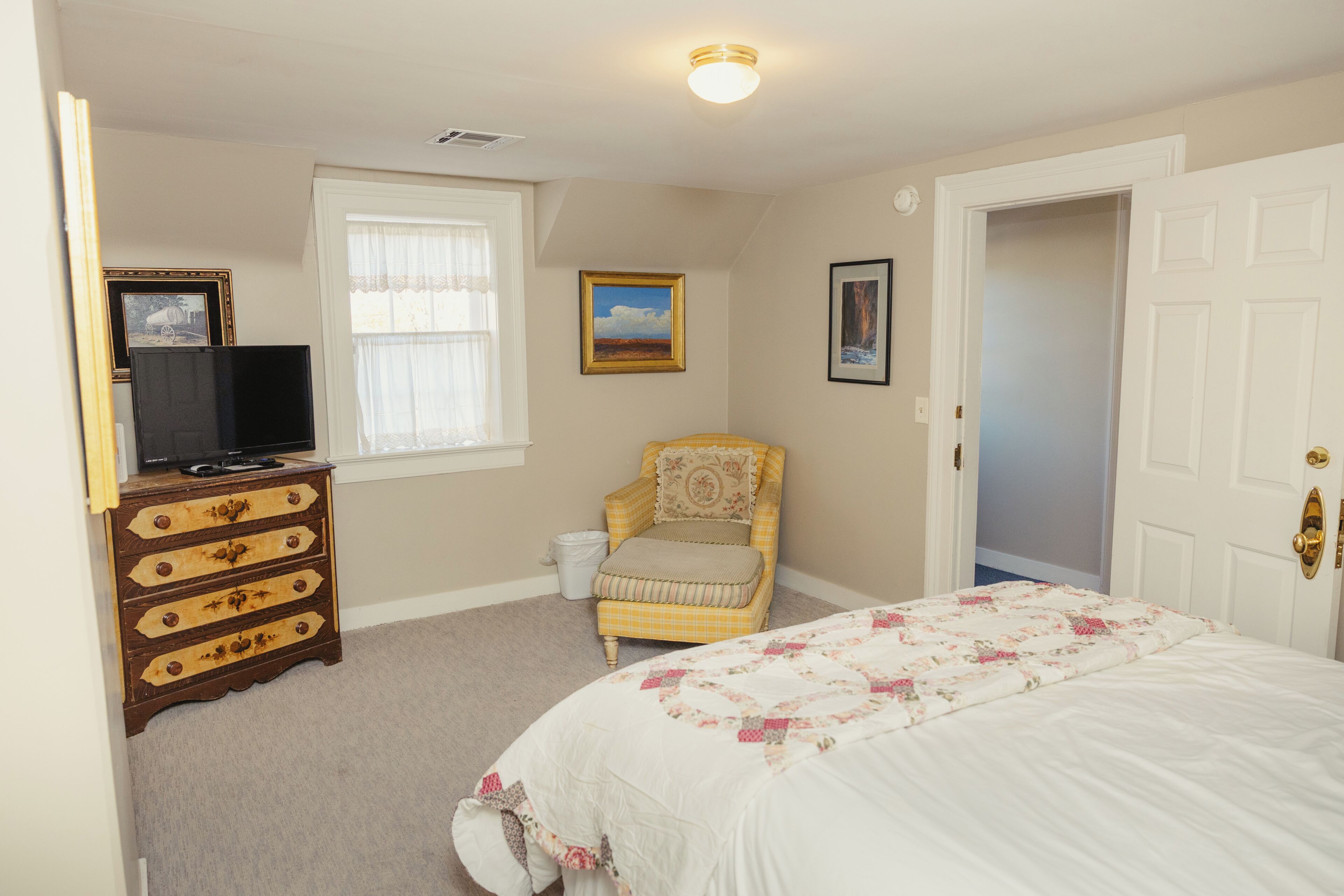 A bedroom with a bed, dresser, chair, and a television.