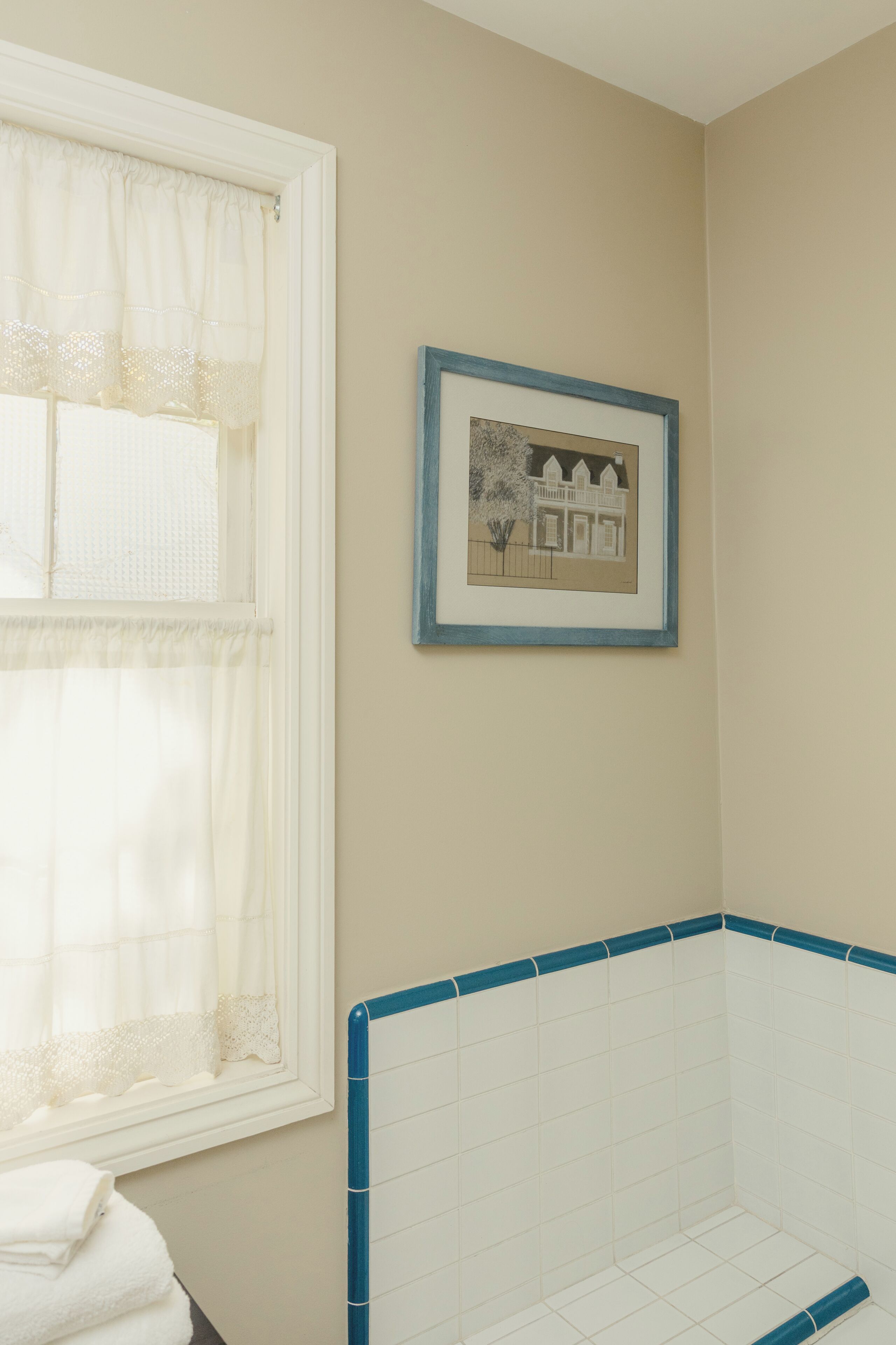 Ein Badezimmer mit einer Badewanne, einem Fenster mit Vorhängen und einem gerahmten Bild an der Wand.