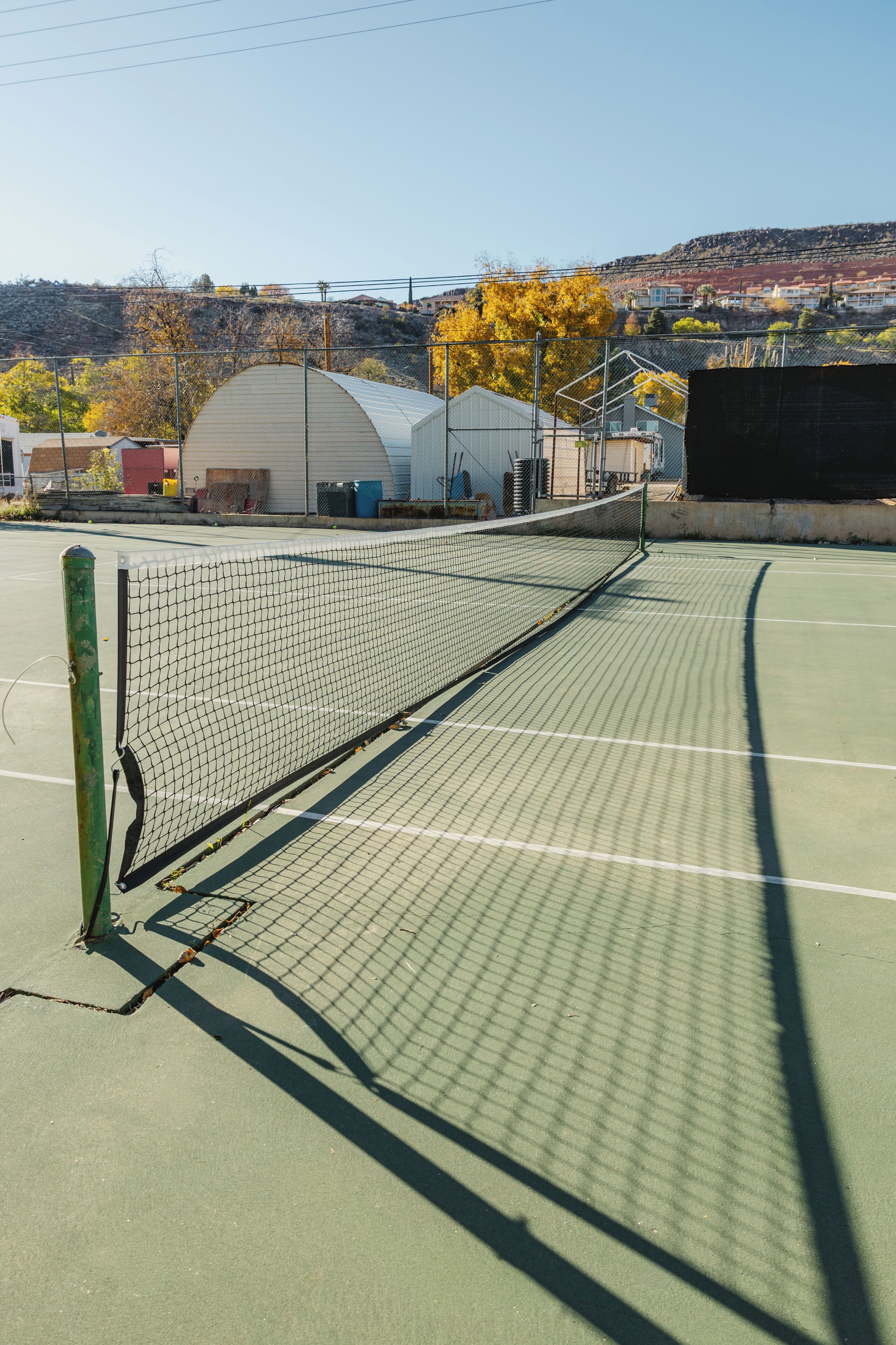 A tennis court with a net, surrounded by buildings and trees.