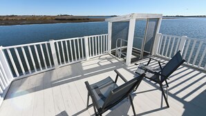 Une terrasse dotée d’une balustrade blanche, de deux chaises et d’un espace clos par des parois de verre, offrant une vue sur l’eau.