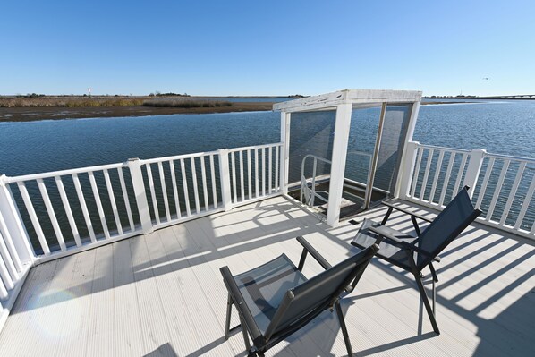 A deck with a white railing, two chairs, and a glass-enclosed area overlooking water.