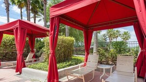A covered outdoor seating area with red canopies, lounge chairs, and a small table. - Gorgeous South-Facing Pool/Spa/Lanai, No Rear Neighbor, Gated Resort Amenities (Davenport)