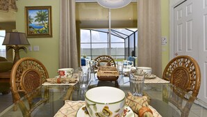 A dining area with a glass table, wicker chairs, and a view through a glass door to an outdoor space. - Gorgeous South-Facing Pool/Spa/Lanai, No Rear Neighbor, Gated Resort Amenities (Davenport)