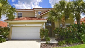 A two-story house with a garage, a small front yard with palm trees and flowering plants, and a clear blue sky. - Gorgeous South-Facing Pool/Spa/Lanai, No Rear Neighbor, Gated Resort Amenities (Davenport)