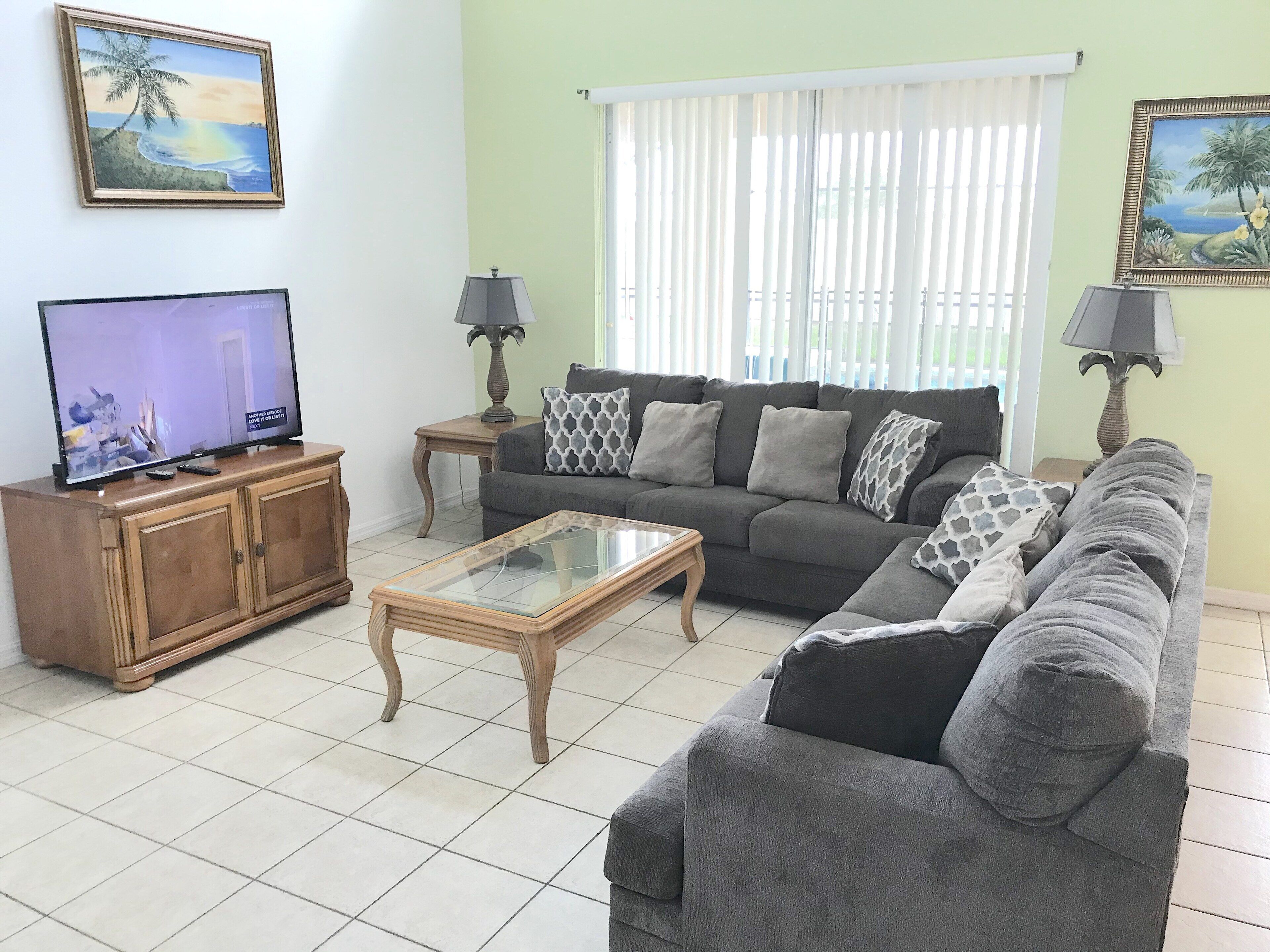 A living room with a sofa, a coffee table, a TV on a wooden cabinet, two lamps, and two paintings on the wall.