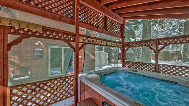 A hot tub in a wooden gazebo with a view of a snowy landscape.