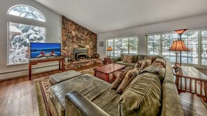 A spacious living room with a stone fireplace, a large sectional sofa, a television, and a ceiling fan.