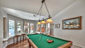 A pool table with a wooden frame, a hanging light fixture, and a framed picture on the wall.