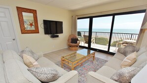 A living room with a sofa set, a glass coffee table, a television, and a balcony with a view of the sea. - Coastal Fantasea - Condo 403: A spacious 2BR retreat in South Padre Island, perfect for 6! (South Padre Island)