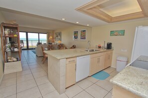A kitchen with a dishwasher, a coffee maker, and a refrigerator. There is a dining area with chairs and a table.