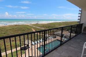 A balcony with a view of a beach and a swimming pool.