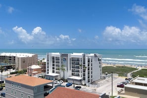 A coastal hotel with multiple floors, a parking area, and a view of the beach and ocean.