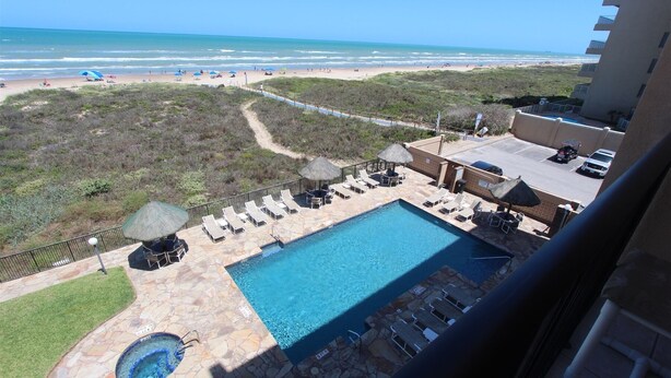 A pool area with lounge chairs and umbrellas, a hot tub, and a view of the beach and ocean. - Coastal Fantasea - Condo 403: A spacious 2BR retreat in South Padre Island, perfect for 6! (South Padre Island)