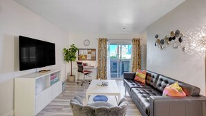 A modern living room with a flat-screen TV, a white coffee table, a gray sofa with colorful cushions, a white cabinet, and a desk with a chair. - Fantastic Strip view walking distance 2br2b condo (Las Vegas)