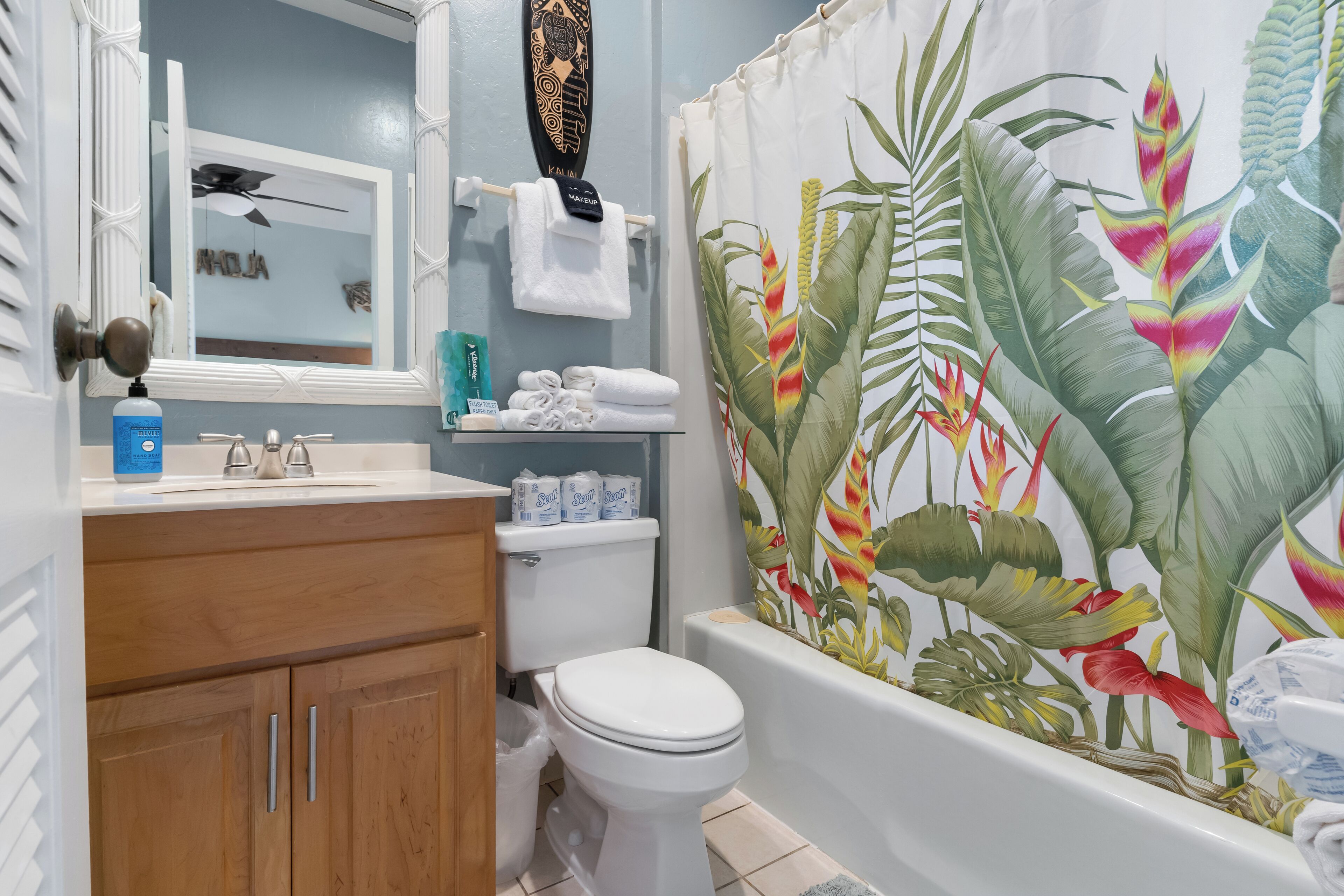 Een badkamer met toilet, wastafel en douchegordijn met tropisch ontwerp.