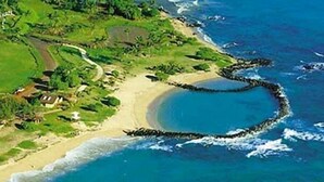 Une vue aérienne d’une zone côtière avec une ligne de rivage incurvée, une plage et une route menant à un ensemble de bâtiments.